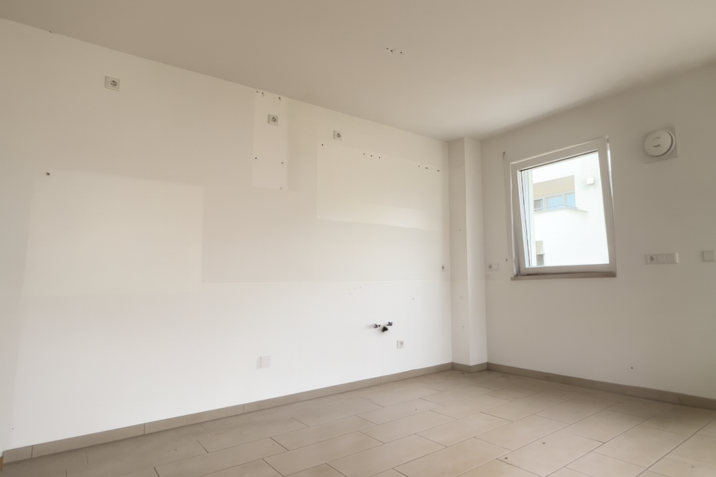 Leere Küche nach Ausbau, weiße Wände mit Bohrlöchern und sichtbaren Anschlüssen.