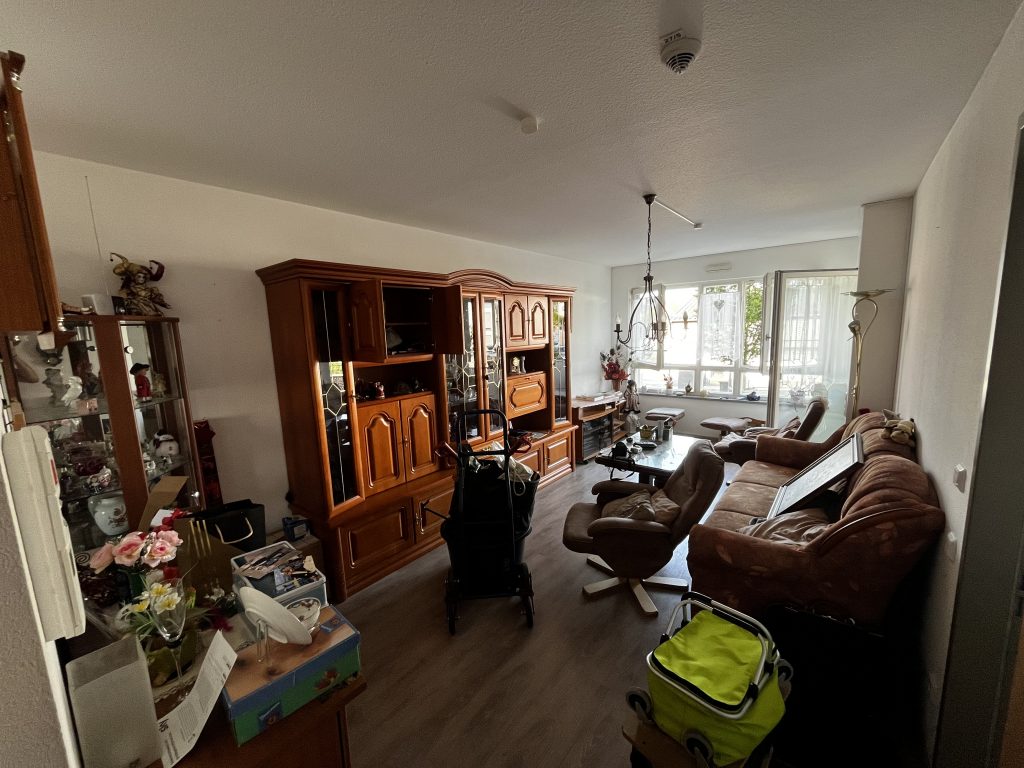 Wohnzimmer mit alten Holzmöbeln, braunem Sofa und voller Einrichtung vor Entrümpelung.