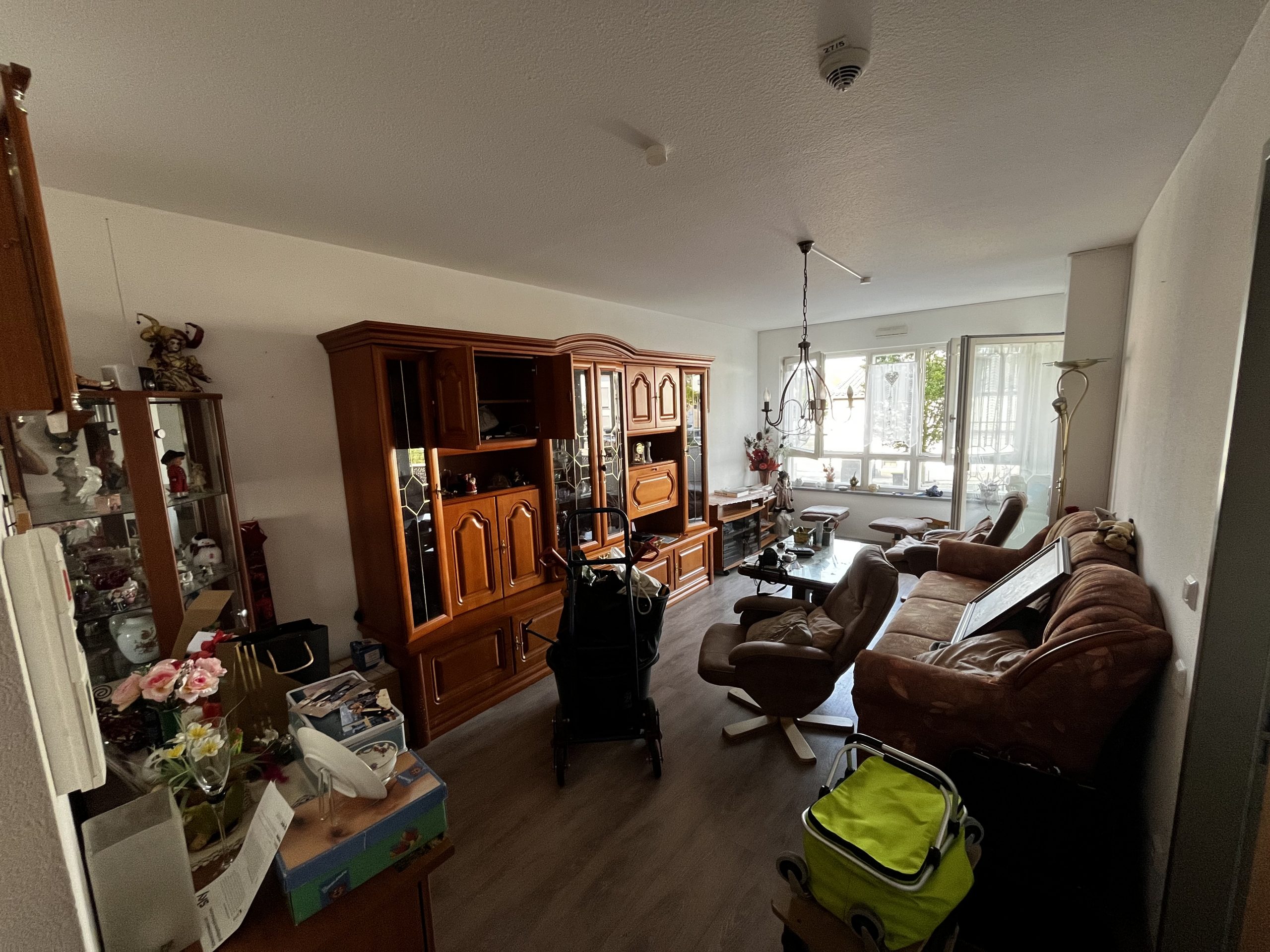 Wohnzimmer mit alten Holzmöbeln, braunem Sofa und voller Einrichtung vor Entrümpelung.