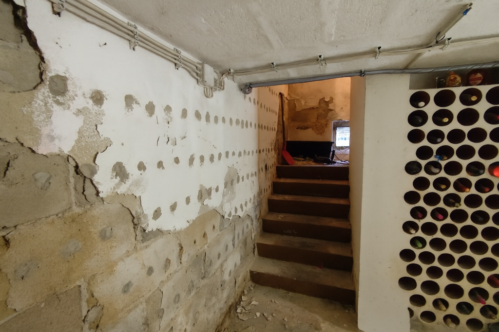 Alter Kellerraum mit beschädigten und abgebröckelten Wänden, kleine Treppe führt nach oben und der Raum braucht Renovierung