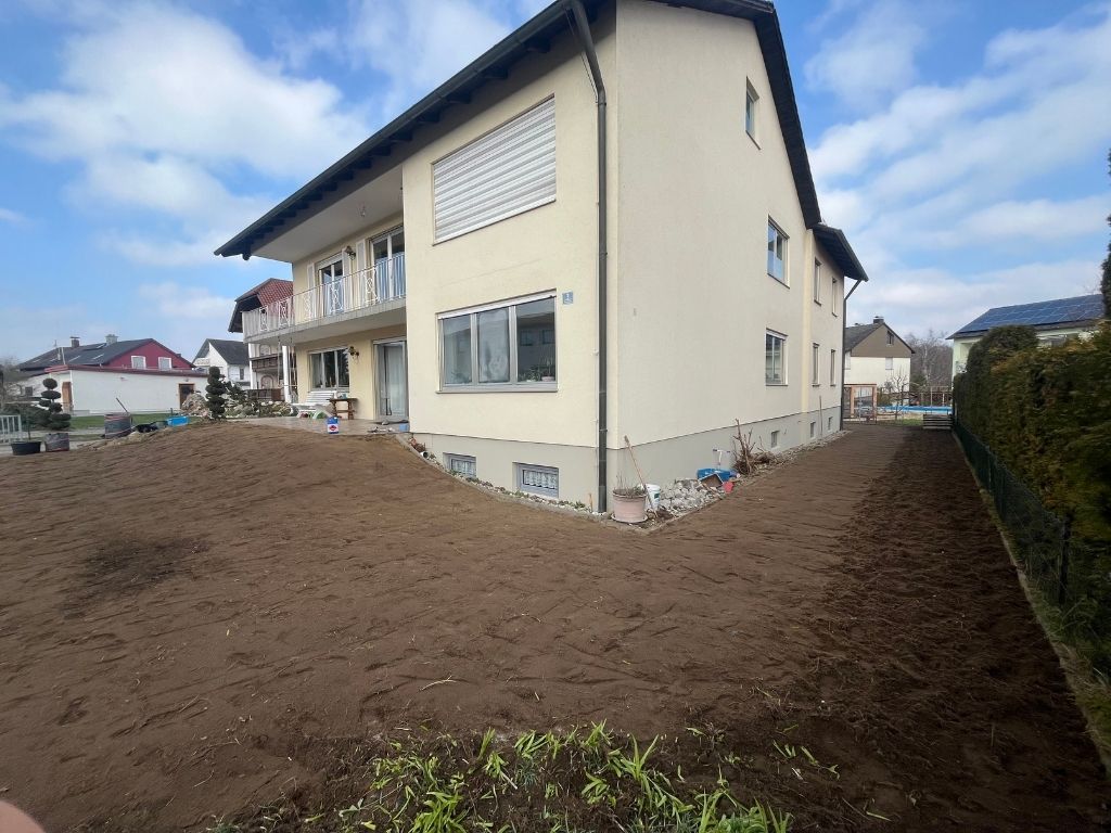Frisch vorbereiteter Gartenboden vor einem Mehrfamilienhaus, bereit zum Verlegen von neuem Rasen.
