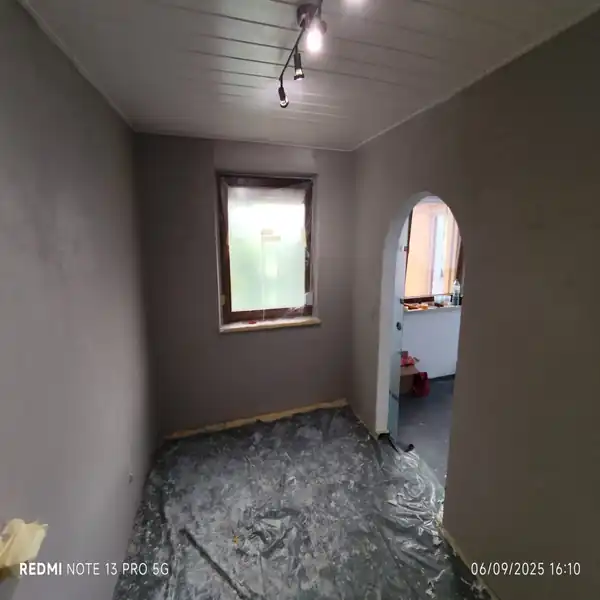 Frisch verputzter Raum mit glatten grauen Wänden und abgedecktem Boden, bereit für den nächsten Renovierungsschritt.